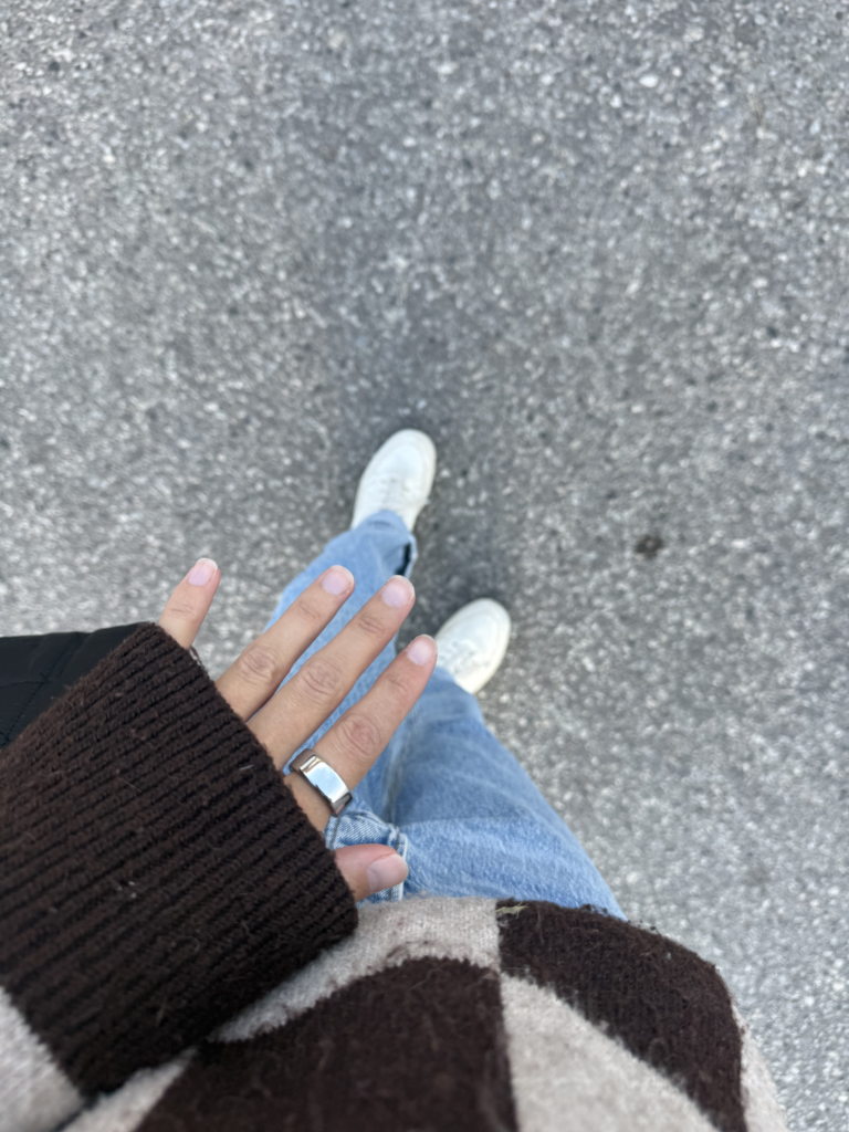 Woman in brown checkered sweater, blue jeans and white sneakers, showing Oura ring